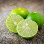 Étiquette du fondant parfumé 'Citron vert' à la cire de soja et fragrance de Grasse. L'illustration montre plusieurs citrons verts frais, dont un coupé en deux, sur une table en bois.