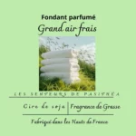 Étiquette du fondant parfumé 'Grand air frais' à la cire de soja. L'illustration montre une pile de serviettes blanches propres dans l'herbe, évoquant le parfum du linge séché au soleil.